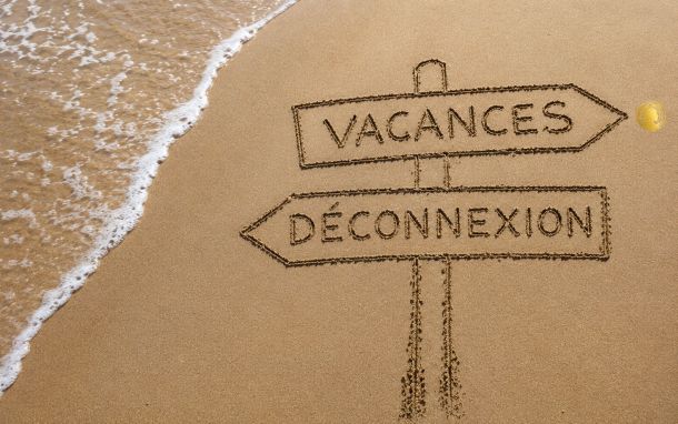 Panneau dessiné dans le sable indiquant vacances et déconnexion pour illustrer le management estival et la dynamique d’équipe pendant les congés